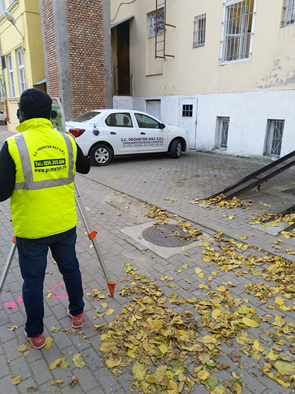 Topograf PROMETER M&G la lucru pe stradă, lângă autovehiculul inscripționat al firmei